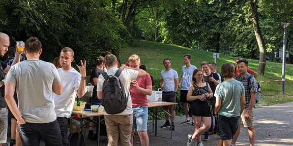 Gruppe von Studierenden steht um einen Grillstand