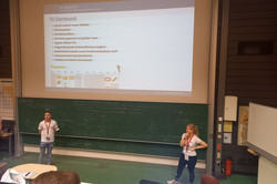 Zwei Fachschaftsmitglieder stellen eine Präsentation im Hörsaal vor