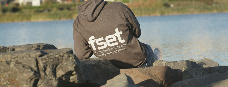 FSR-Mitglied von hinten am Ufer sitzend, Pullover ist hinten mit Logo bedruckt