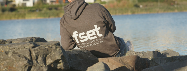FSR-Mitglied von hinten am Ufer sitzend, Pullover ist hinten mit Logo bedruckt