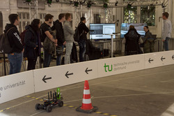 Gruppe von Studierenden bekommt eine Rennstrecke für eine Robotikplattform mit dem Steuerplatz erklärt