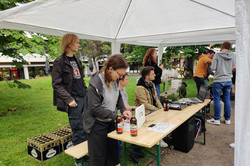 Drei Studierende sitzen auf einer Bank, zwei davon hinter einer Kasse und einer hinter einem DJ-Mischpult