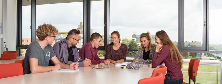 Six students are sitting at a table with books and notepads on.