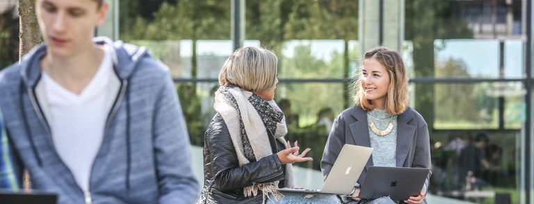 Two students sitting on a bench are talking to each other