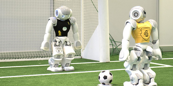 Ein Roboter mit schwarzem Trikot steht in einem Fußballtor und ein zweiter Roboter steht mit einem Ball am Elfmeterpunkt.